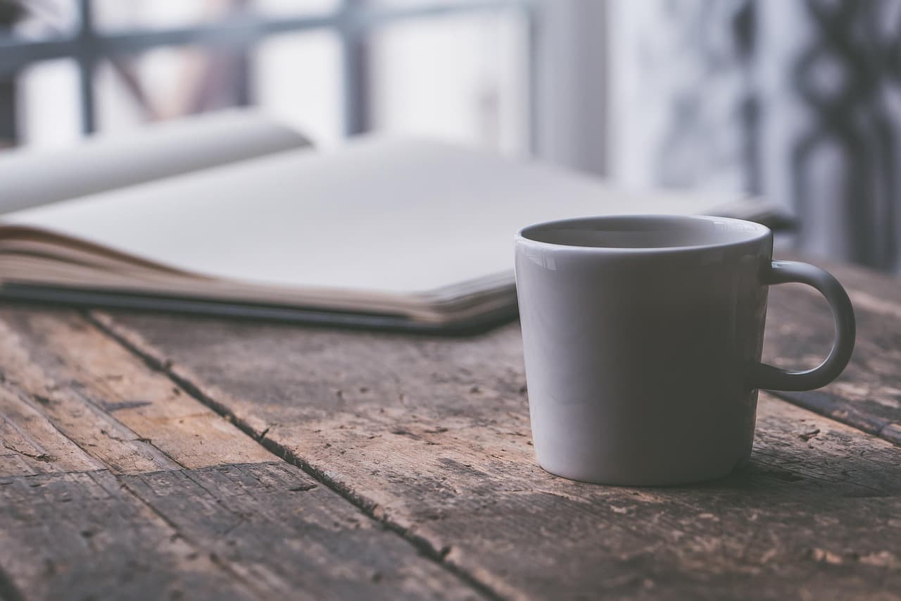 A grey mug on a weathered wooden table beside an open notebook