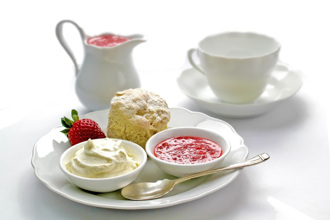 A scone with clotted cream, strawberry jam and a jug of cream beside a teacup