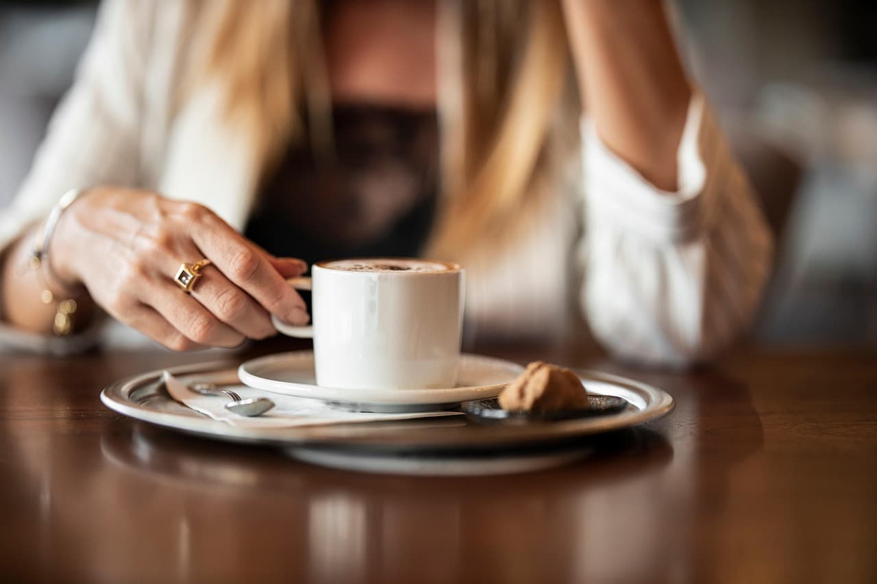 A woman's hands either side of a cup of coffee on a saucer at a cafe table