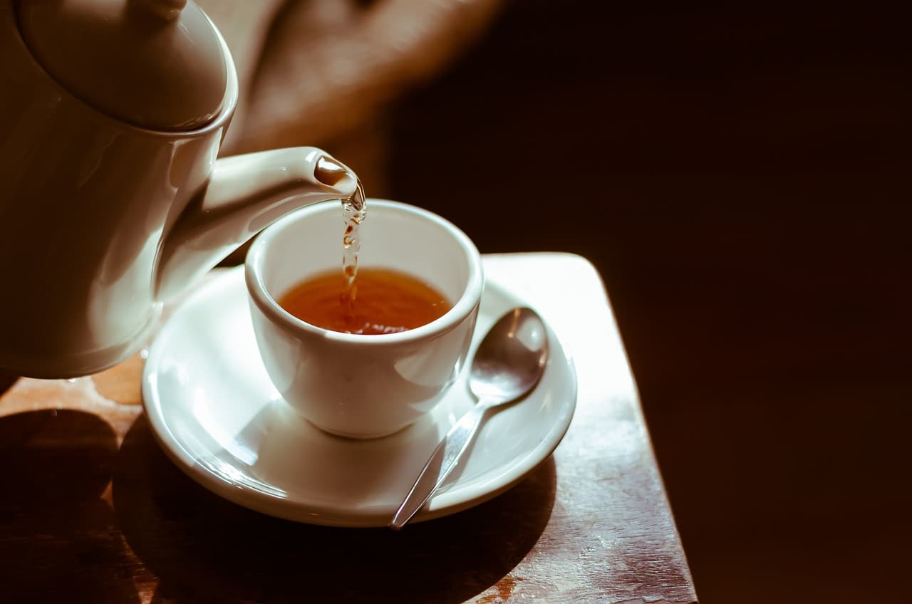 Tea being poured from a pot into a cup on a saucer, in warm low light