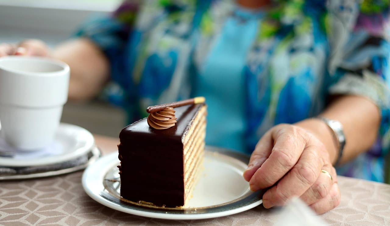 A slice of layered chocolate cake on a plate, with a cup of coffee