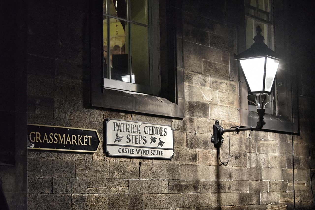 An old stone wall in Edinburgh with a lamp and signs for the Grassmarket and Castle Wynd steps
