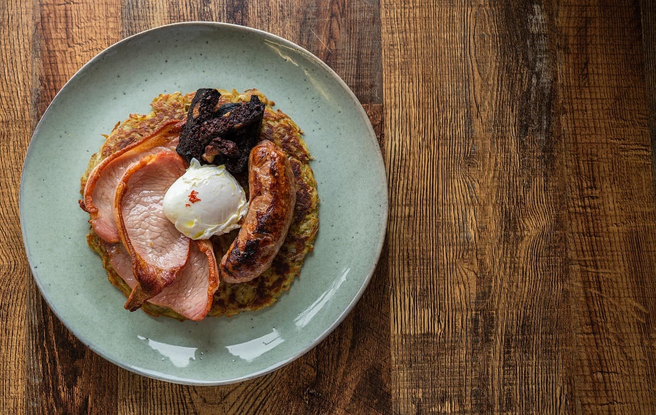 Bacon, a sausage, black pudding and a poached egg on a green plate on a wooden table